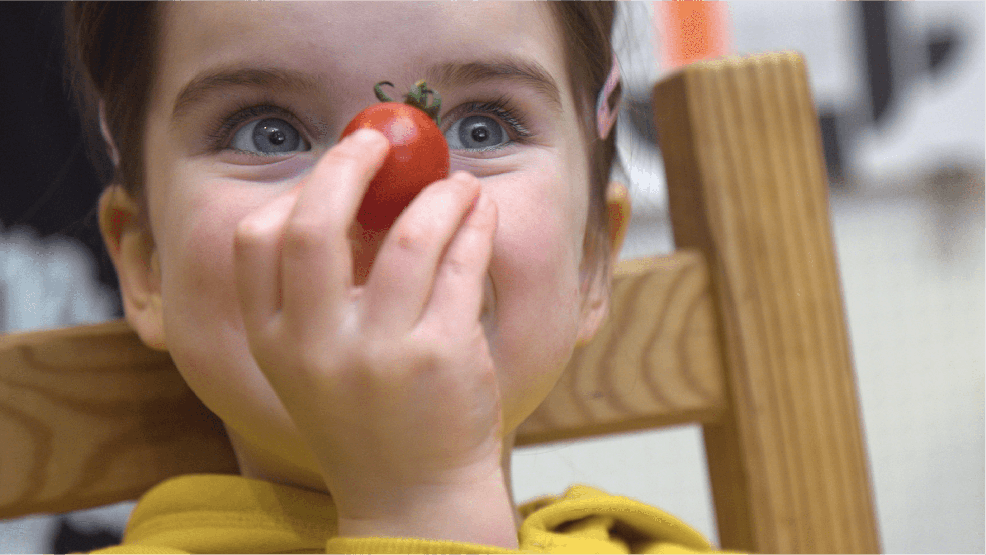 A child holding a cherry tomato in front of her nose