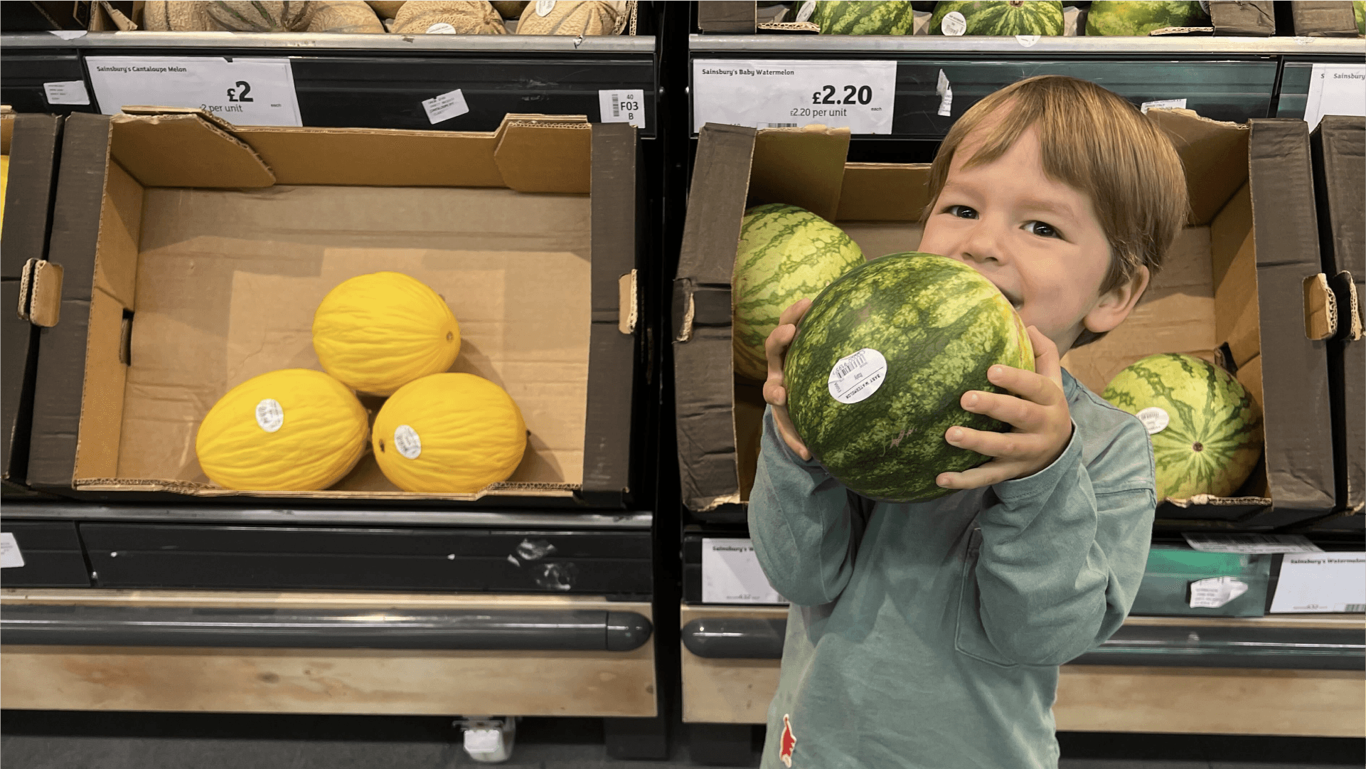 A boy holding a watermelon in a supermarket