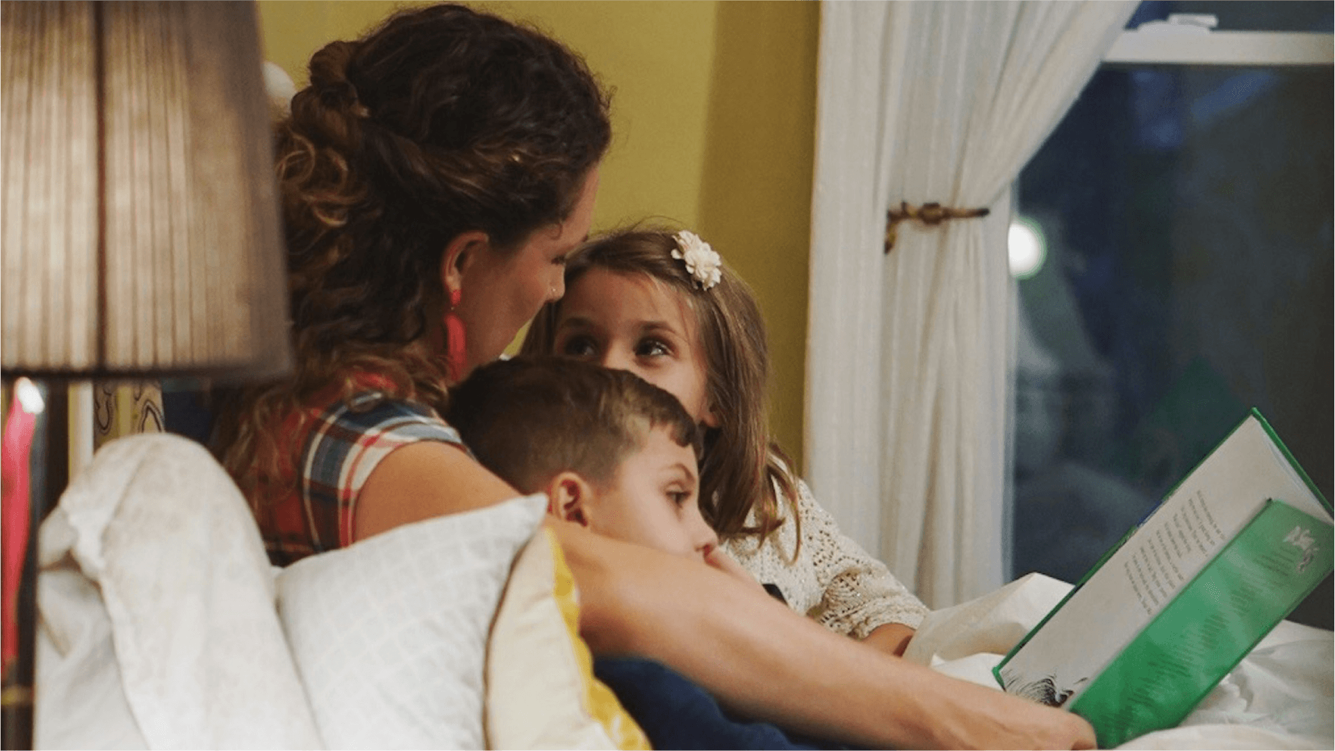 A parent reads to two kids in bed