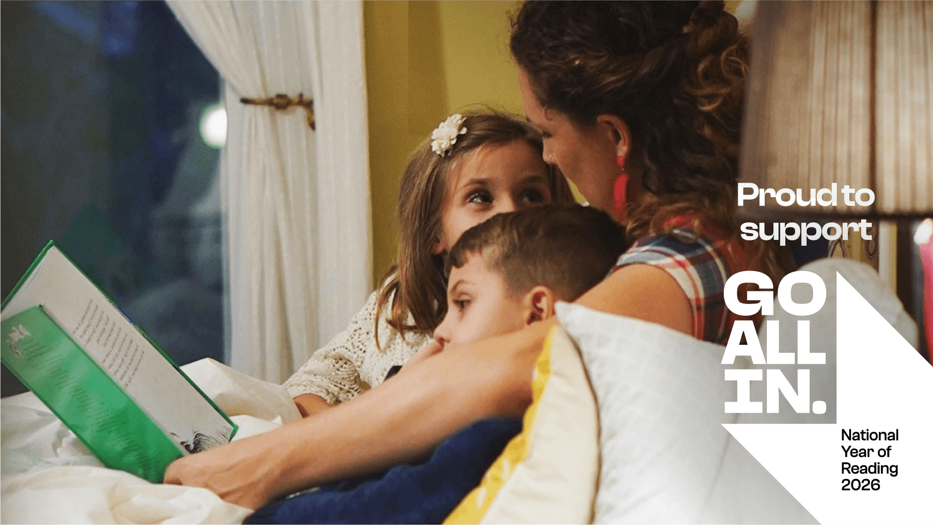 A parent reads to two kids in bed